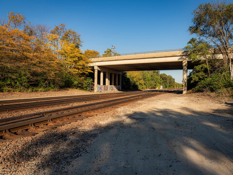 Concrete highway overpass bridge spanning railroad tracks lined with autumn trees under a clear blue sky   