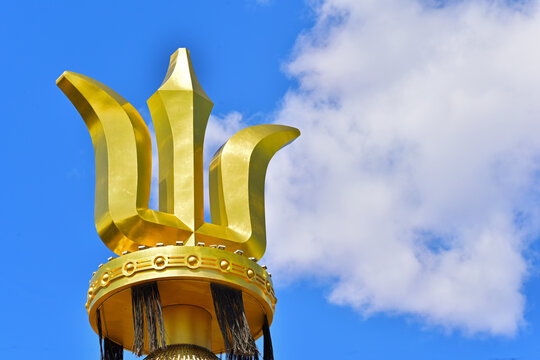 Golden Three-Pronged Ornament on Pole Against Blue Sky