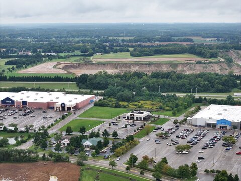 Aerial view of a commercial shopping center featuring a Lowe's and a Walmart, with large parking lots, surrounding green spaces, and a nearby field in Xenia, Ohio, United States.