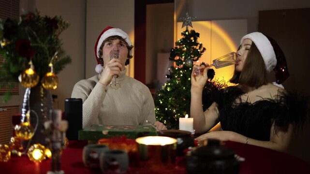 Christmas dinner feels cold and distant as an upset couple drinks champagne in silence after an argument avoiding eye contact despite the warm festive atmosphere around them