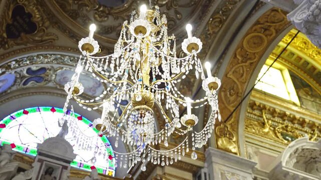 An illuminated crystal chandelier hangs beneath a painted ceiling amid gilded arches, stained glass and carved stone decoration.