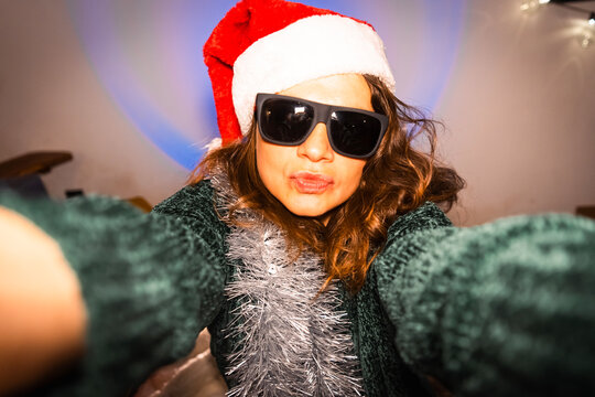 Funny young woman in Santa hat and sunglasses taking a selfie with smartphone on Christmas.