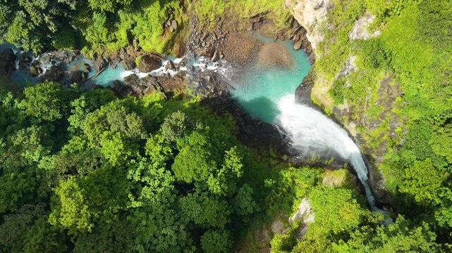 High angle top down view with parallax effect as camera moves sideways over Victoria Falls plunging into turquoise pool surrounded by lush tropical forest