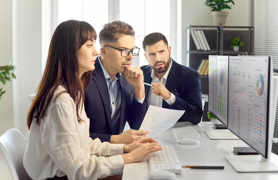 Analysts teamwork in office analyzing data. Colleagues compare finance charts on two monitors, evaluate trends, adjust reports and align strategy with goals. Clean concept of team analytics.
