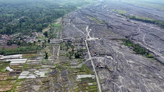 Top down birdseye sky perspective capturing deeply cracked mud plains and eroded infrastructure footprints left behind long after the initial volcanic mudflow crisis.