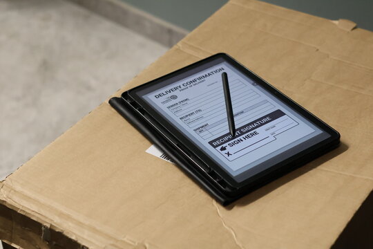  Person signing electronic proof of delivery form on a digital tablet near a doorway, using a stylus to confirm package receipt. Concept of contactless delivery, logistics management, courier service,