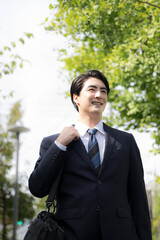  屋外の道路を歩きながら営業の外回りや取引先への訪問に向かうスーツ姿の日本人男性サラリーマン、法人営業や転職のイメージクローズアップで見上げる縦 © kapinon