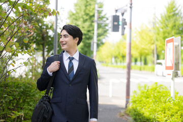 屋外の道路を歩きながら営業の外回りや取引先への訪問に向かうスーツ姿の日本人男性サラリーマン、法人営業のイメージ上半身 © kapinon