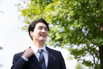  屋外の道路を歩きながら営業の外回りや取引先への訪問に向かうスーツ姿の日本人男性サラリーマン、法人営業や転職のイメージクローズアップで見上げる © kapinon