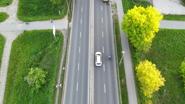 Aerial view of vehicles traveling on a multi-lane road surrounded by lush greenery, showcasing the flow of traffic and the vibrant landscape in the background. Cars riding at rural route