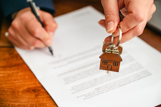 Real estate agent holding house keys above property contract