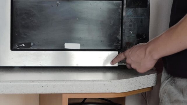 Person opening a microwave oven door in a modern kitchen setting