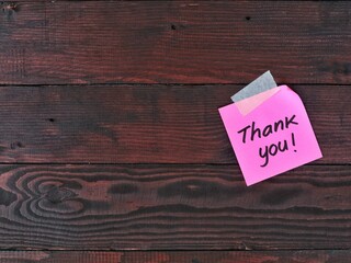 Handwritten thank you message on pink adhesive note paper taped on dark wooden texture background with copy space. Concept for gratitude, customer service, appreciation, feedback, and support message © Eka