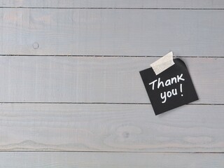 Handwritten thank you message on black adhesive note paper taped on grey wooden texture background with copy space. Concept for gratitude, customer service, appreciation, feedback, and support message © Eka
