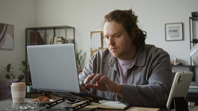 Caucasian young adult man typing on laptop and writing notes in notebook at desk. Perfect for remote work, e-learning courses, software programming, freelance business promotional videos