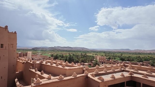 high-angle panoramic overlooking historic mud brick Kasbah ramparts and towering structures stretching toward a vast green date palm plantation under a dramatic cloudy sky in Ouarzazate