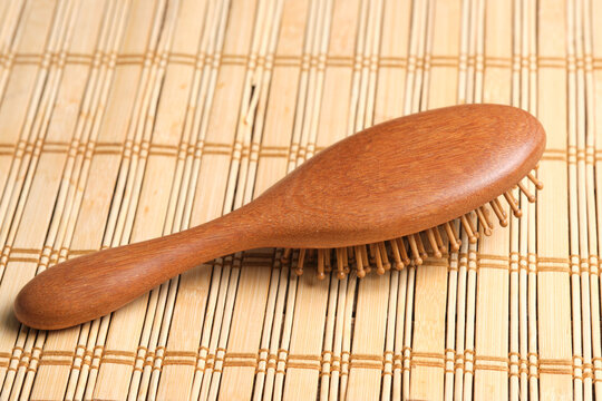 Natural wooden hairbrush lying smooth back side up on textured bamboo mat background.