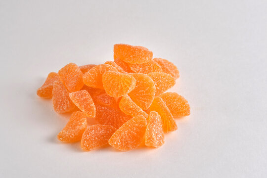 Pile orange citrus shaped marmalade candies sprinkled with sugar placed on clean white surface.