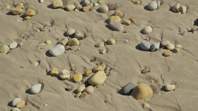 Close-up shot of smooth rounded pebbles and stones scattered across rippled wet sand on a scenic beach in Ribadesella Asturias Spain.