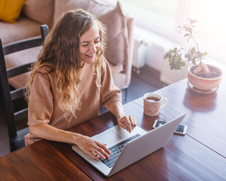 Woman working on laptop at home while enjoying a cup of tea. Remote work and flexible employment. Digital communication and online business. Comfortable home office lifestyle.