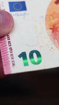 Defocused vertical video close up. Bank note. Hand holds edge of 10 euro paper banknote with green emerald number value, EU flag. Cash money of European Union, Europe. Pay credit, tax, debt, loan. Buy