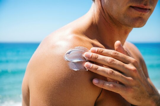 Hombro y mano de un hombre extendiendo crema solar blanca sobre una piel ligeramente bronceada por el sol
