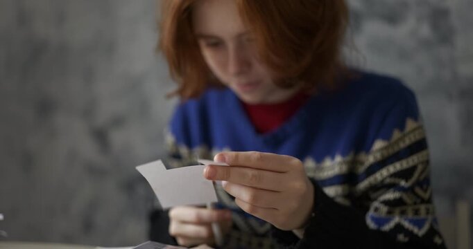 Scotland red-haired young person in a blue patterned sweater carefully cutting paper with scissors, soft focus, shallow depth of field, moody gray background. Ideal for craft and creativity themes