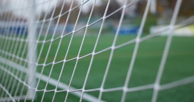 Cinematic football footage white goal net in sharp focus with an empty green artificial turf pitch softly blurred behind. Soccer sport, empty stadium field, shallow depth of field, autumn day, 4K clip