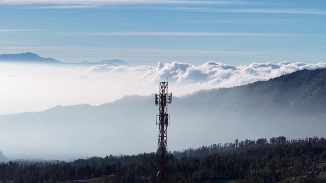 Telecom tower piercing misty mountain ridges beneath dramatic cloud inversion.