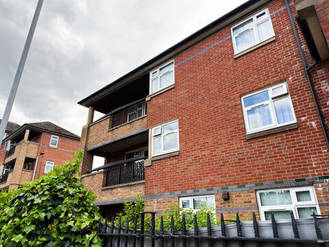Residential brick apartment building with balconies, iron fence and greenery in Manchester, UK under cloudy sky