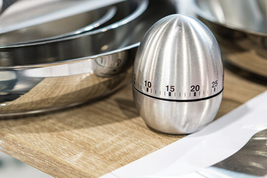 Kitchen timer on wooden cutting board, presenting metallic surface with brushed finish, circular dial markings, warm wood tones, clean modern style, slight shadows and reflections