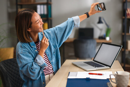 Young woman taking a smartphone selfie at her home office desk