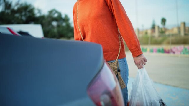 Woman open trunk of parked car and placing shopping bags filled with fruit inside. Everyday errands, household responsibilities, independent living, personal transportation, practical daily activities