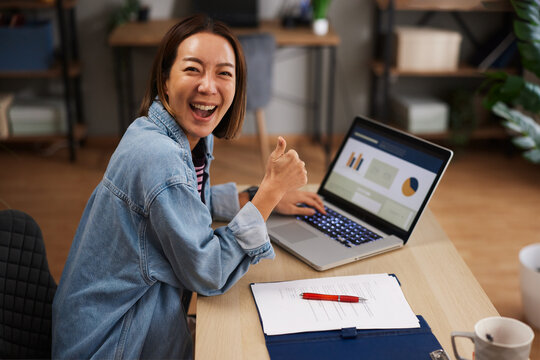 Asian woman celebrating remote work success with laptop