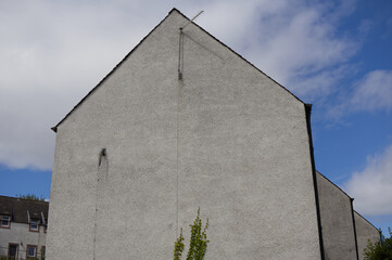 Gable wall of a residential house with traditional roughcast pebbledash stucco facade and TV antenna against blue cloudy sky in Stirling, Scotland, UK © TomKorcak