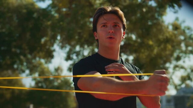 Man performs controlled resistance band training and torso rotations during an outdoor strength workout in a sunny park.