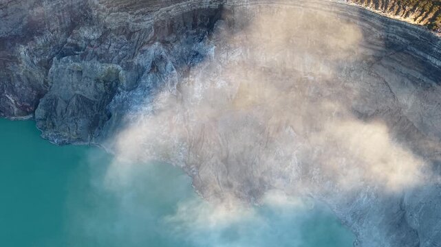 Top down drone shot of Mount Ijen crater lake with turquoise water and drifting sulfur steam