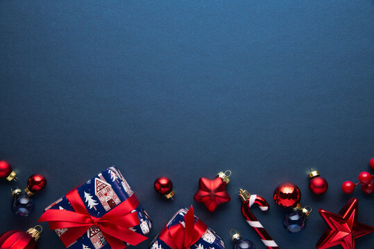 Blue Christmas and Happy New Year holiday background with gift boxes, red ribbon bows and festive red ornaments, flat lay with copy space. Greeting card.