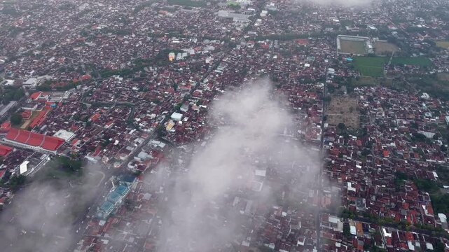 High altitude urban panorama showing dense rooftops, town fields and misty clouds over Banyuwangi city.