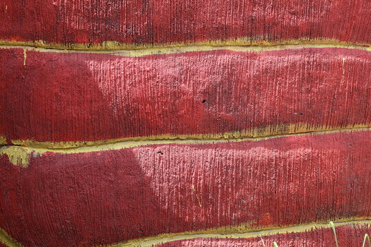 Rough maroon painted cement wall creates a unique decorative textured background surface.