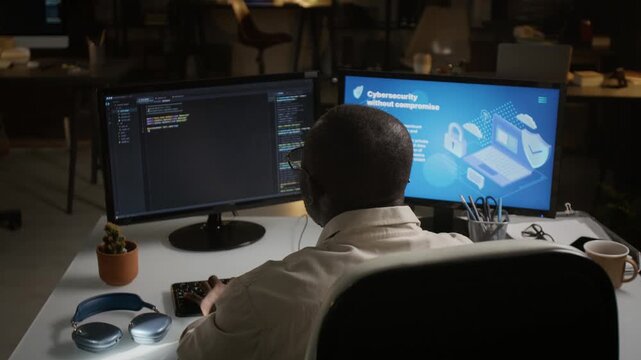 African American young adult developer coding on dual monitors with cybersecurity interface. Ideal footage for data protection commercials, IT corporate presentations, tech ads