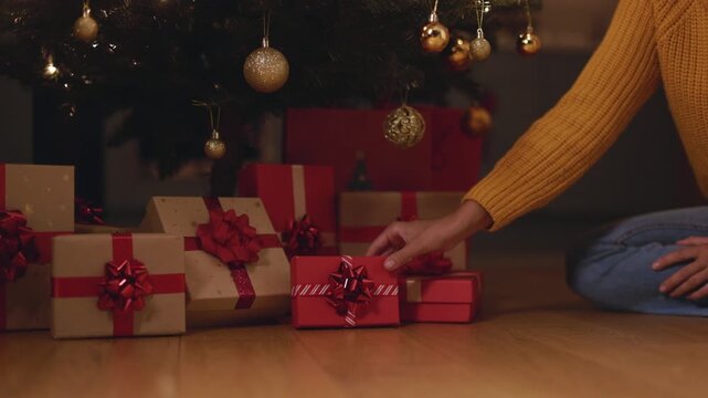 Woman placing Christmas gift box with decorative bow beneath festive tree, 4K