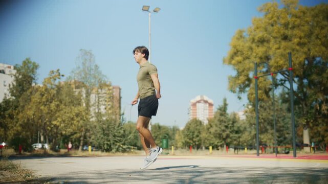 Man jumps rope on an outdoor court, pauses to wipe sweat and breathe, then resumes cardio exercise in a tracking shot.