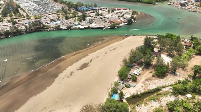 Aerial view of the Cilacap Shrimp Farm located near the river mouth and sandy beach, featuring small structures, lush trees, and coastal waters in Nusawungu, Central Java, Indonesia.