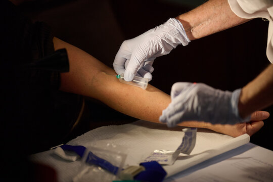 Healthcare worker collecting a blood sample from a patient's arm with a vacuum tube holder during a medical procedure