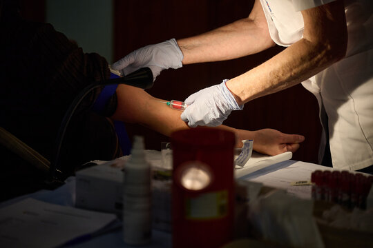 Medical professional drawing blood from a patient's arm using a vacuum tube collection system during a clinical examination