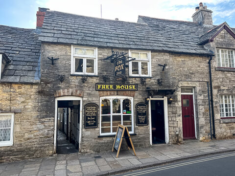 Corfe Castle, Dorset, UK - July 13, 2026. The Fox Inn Historic Stone Pub Facade on Corfe Castle Street. A high-detail horizontal photograph capturing the rustic Purbeck stone facade of The Fox Inn fre