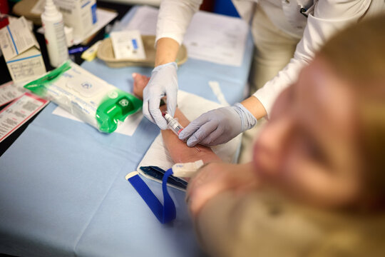 Healthcare professional preparing to draw blood from a patient's arm using a collection tube in a clinical medical setting