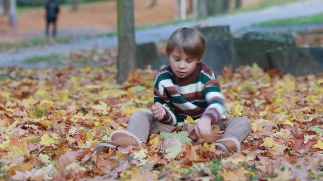 Cute blond child in the park, playing with knitted pumpkins, autumn time