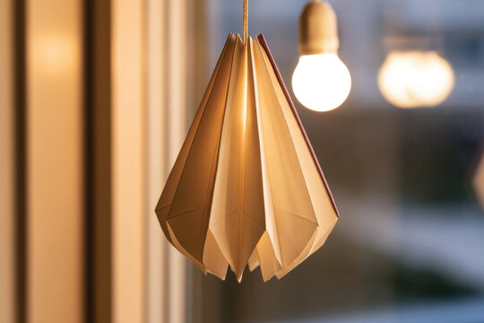 A beautifully crafted paper light fixture, suspended by the window, blending artistry and illumination, enhancing the aesthetic appeal of the surrounding space.